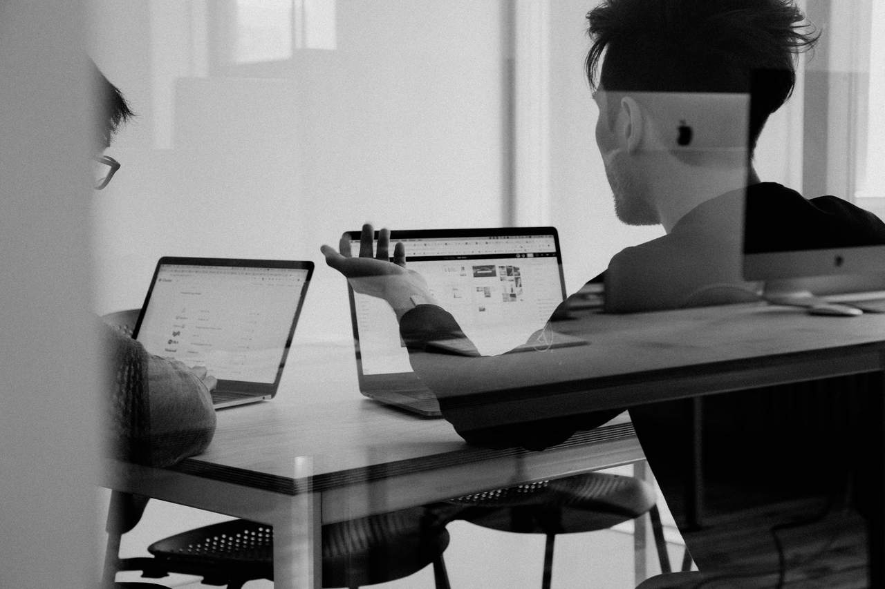 Two colleagues at a desk, one explaining something, in black and white