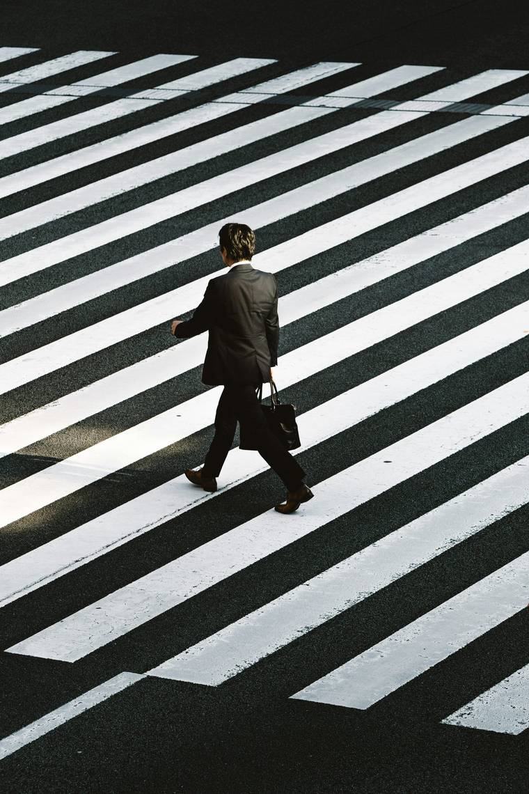 A single person crossing a wide zebra crossing, alone among dozens of identical stripes